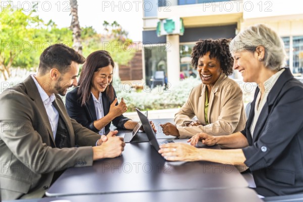 Side view of multi-ethnic happy business people in a meeting using laptop sitting in a cafeteria