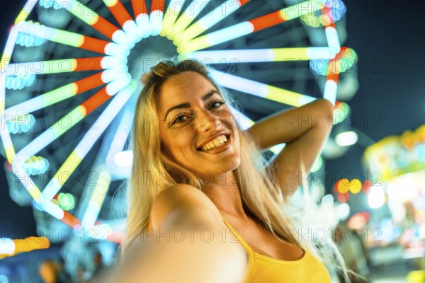 Personal point of view of a beauty happy woman taking selfie in an amusement park at night with a big wheel on the background illuminated by neon lights