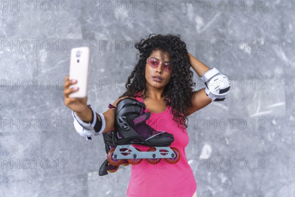 Latin woman in sportswear and protective gear taking selfie holding inline skates outdoors