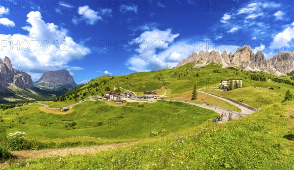 Stunning landscape of gardena pass in the italian dolomites, featuring lush meadows, winding roads, and majestic peaks under a bright blue sky