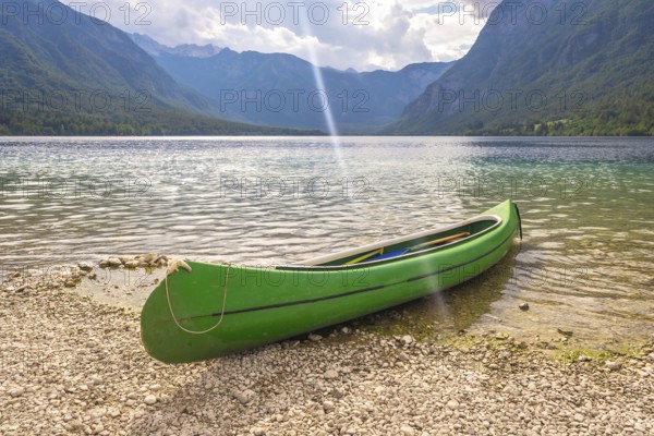 Green canoe resting on the pebbled shore of lake bohinj, with the julian alps in the background, offering a serene view of nature's beauty