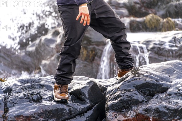 A person is standing on a rock with their feet in the water. The water is flowing down a waterfall