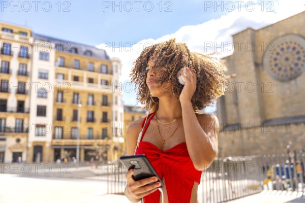 Cool latin woman with curly hair dancing and listening to music in the city