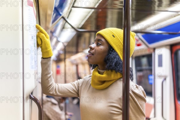 Tourist wearing yellow winter clothes checking subway map while traveling inside metro train