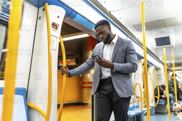 Young businessman in suit using his smartphone while entering a subway train, holding the handrail