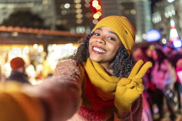 Smiling woman wearing winter clothes showing victory sign holding boyfriend's hand enjoying christmas market at night