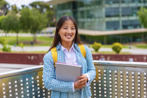 Portrait of a cheerful asian student smiling at camera standing in the university campus