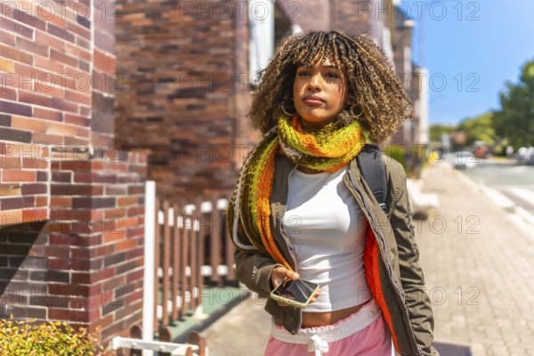 Latin beauty woman using phone while walking along street with bag and warm clothes