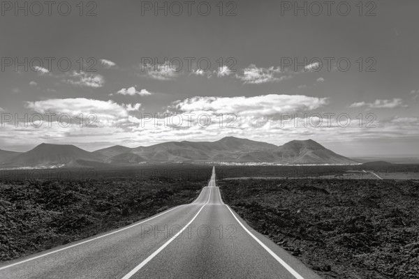 Empty endless country road through volcanic landscape, typical lava fields, Timanfaya National Park, fire mountains on the horizon, monochrome, Lanzarote, Canary Islands, Spain, Europe