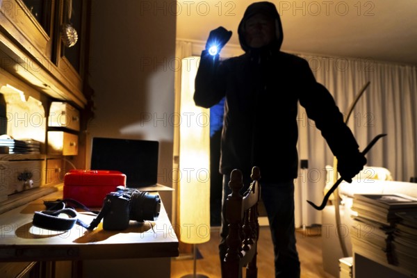 Symbolic image of a burglary, perpetrator has broken into a flat from the garden side and is looking for loot, cash box, valuables, money, technology