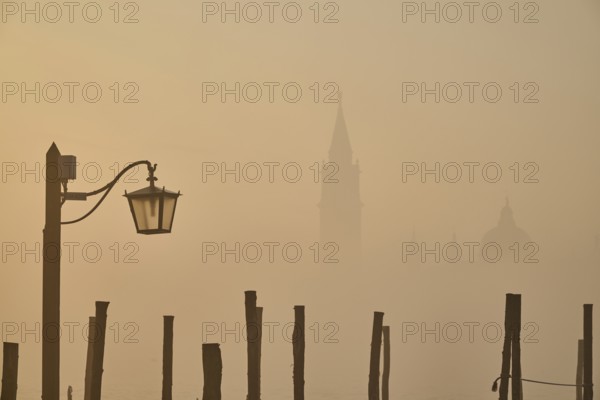 View from 'Colonna di San Marco e San Teodoro' on church 'Giorgio Maggiore' on a foggy morning at sunrise with a latern in front in Venice in winter, Italy, Europe