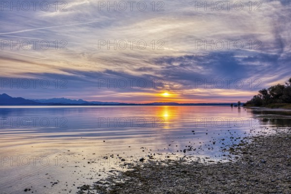Calm lake reflects a colourful sunset with clouds and shore, Chiemsee