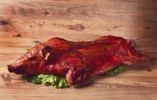 Baked, fried piglet, on a wooden table, no people, The whole piglet is baked and served on the leaves of a fresh green salad, showing off its crispy skin and detailed features