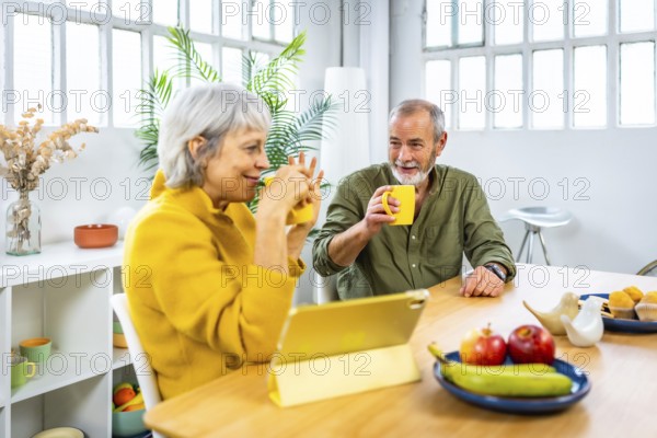 Senior couple using tablet while drinking coffee at home during breakfast in the morning