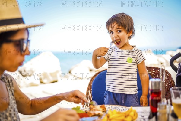 Mother and son enjoying a delicious meal together at a beachside restaurant during their summer vacation
