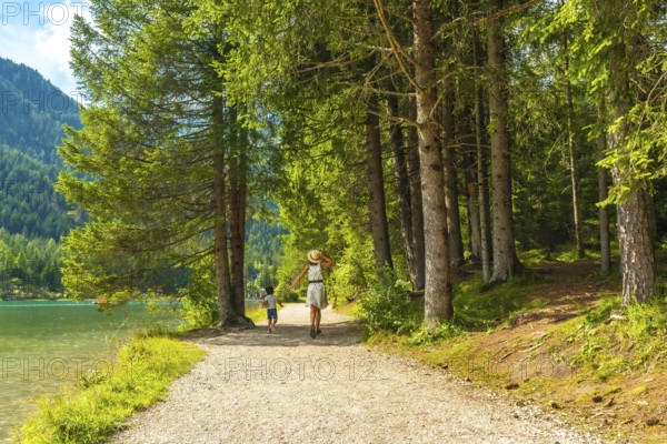 Tourists enjoying the stunning landscape of the dolomites while walking on a gravel path by the lake in the woods