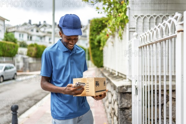 African delivery man using mobile while holding cardboard package to deliver