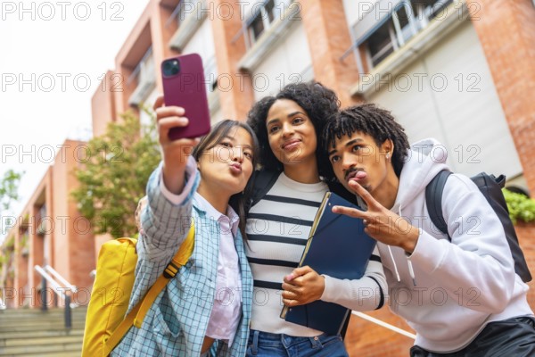 Low angle view portrait of three happy multiracial university students taking a selfie outside the campus