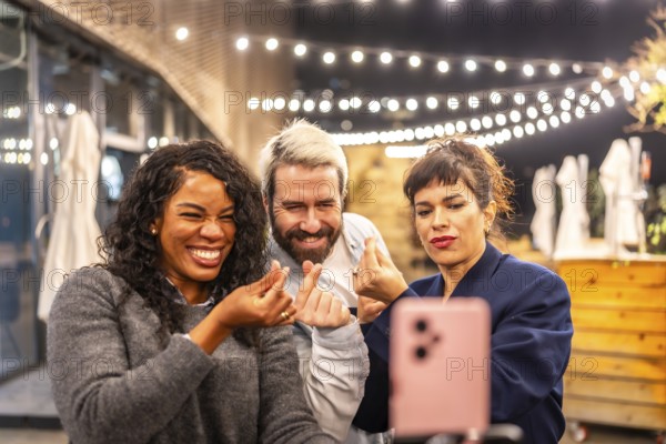 Multiracial diverse friends streaming online with a smartphone and gesturing love during night party