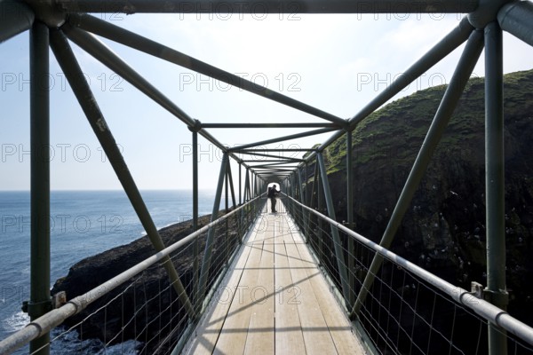Hiker standing on the so-called Atlantic Bridge, footbridge over a crevice Hólmgjógv, Mykines, Útoyggjar, Faroe Islands, Denmark, Europe
