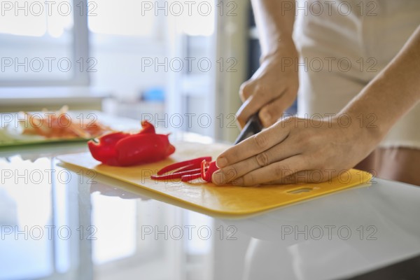 A person is slicing fresh red bell peppers on a yellow cutting board in a well-lit kitchen