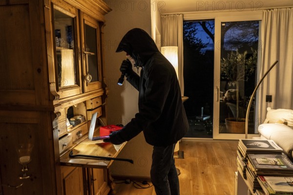 Symbolic image of a burglary, perpetrator has broken into a flat from the garden side and is looking for loot, computer, laptop, valuables, money, technology