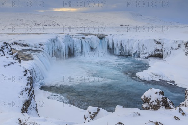 Icy waterfall and rapids in front of a mountain landscape, cloudy mood, snow, Godafoss, Iceland, Europe