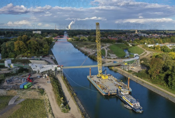 Castrop-Rauxel, North Rhine-Westphalia, Germany, new construction of a bridge -jump over the Emscher-, a floating crane on the Rhine-Herne Canal floating in the centre section of a foot and cycle bridge over the Emscher and the Rhine-Herne Canal. EMSCHERLAND construction project, a 37-hectare water and nature adventure park at the water crossroads of the Rhine-Herne Canal (right) and the renaturalised Emscher (from right to left) on the city boundary between Recklinghausen and Castrop-Rauxel. EMSCHERLAND will also be a garden of the future for the International Garden Exhibition 2027. Before the renaturalisation, the Emscher river system was an open, above-ground wastewater canal, mixed water canal with surface water and wastewater. The Uniper power plant Datteln 4 in the background, Europe