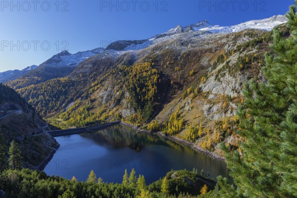 The Galgenbichl reservoir with a mountain forest in fall foliage on a bright sunny morning. Seen from the Malta Hochalm road. Carithia, Austria, Europe