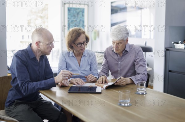 Symbolic photo on the subject of counselling. An older woman and an older man sit together at a table at home and receive counselling from a young man. Berlin, 13.08.2024