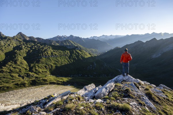 Mountaineer in front of mountain landscape at sunrise, view of mountain peaks of the Venediger group and into the Großbachtal valley from the summit of Bachlenkenkopf, Lasörling group, Hohe Tauern National Park, East Tyrol, Tyrol, Austria, Europe