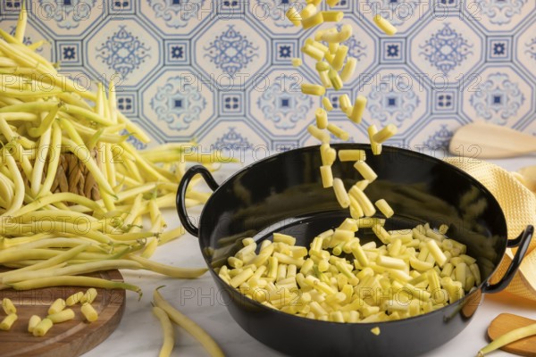 Sliced beans fall into a cooking pot on a kitchen worktop, whole runner beans in the background