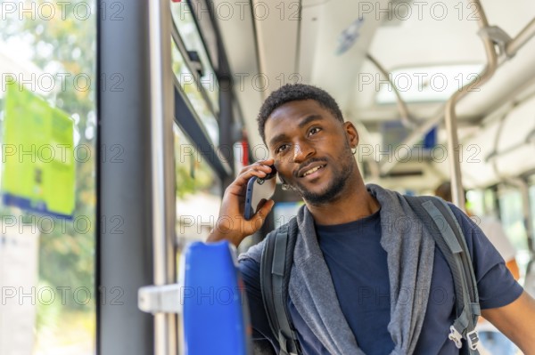 African young man talking to the mobile sitting in an urban bus