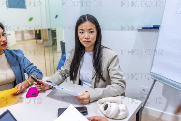 Young asian businesswoman leading a meeting with colleagues in a modern coworking office, discussing paperwork and strategies