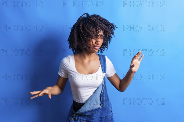 Young woman wearing casual clothes dancing with joy and moving her curly hair on a vibrant blue background