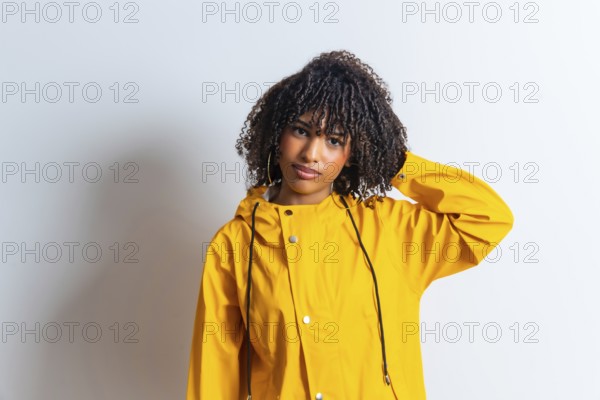 Studio portrait of a young woman wearing a yellow raincoat and scratching her head against a white background