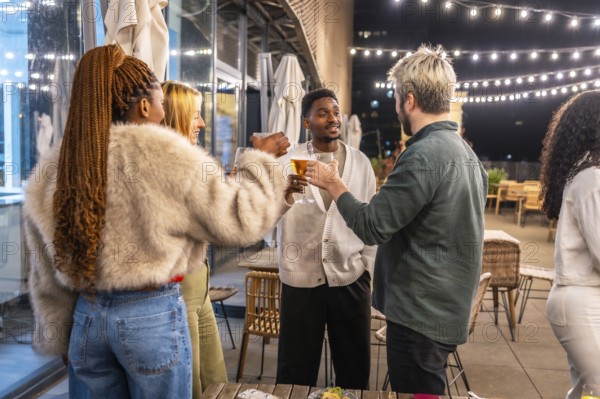 Group of young multi-ethnic friends toasting standing on a bar terrace at night