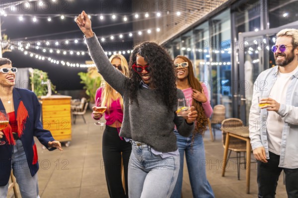 Latin woman celebrating dancing with friends at night in the terrace of a modern city bar