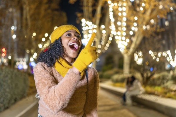 Excited young woman pointing her finger to christmas lights decoration in a city park at night