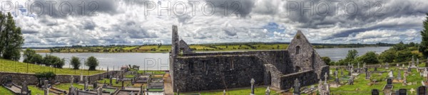 Ruin by a river with gravestones and cloudy sky in a rural setting, Urlaur Abbey