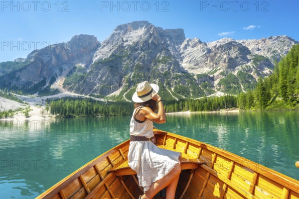 Young woman wearing a straw hat enjoying a boat trip on the turquoise waters of lake braies with the dolomites in the background during a summer day