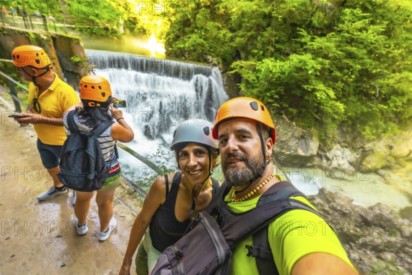 Hikers wearing helmets are taking a selfie with a waterfall in the background at vintgar gorge near bled, slovenia