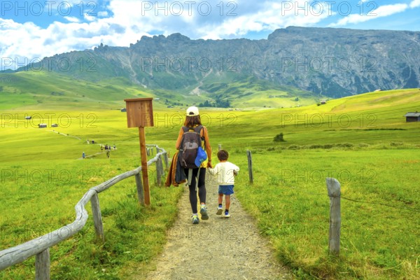 Tourists enjoying a scenic hike in the beautiful alpe di siusi, surrounded by the stunning mountain landscape of the italian dolomites