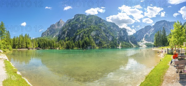 Tourists enjoying the breathtaking panorama of lake braies with its crystal clear turquoise waters reflecting the majestic dolomites on a sunny summer day