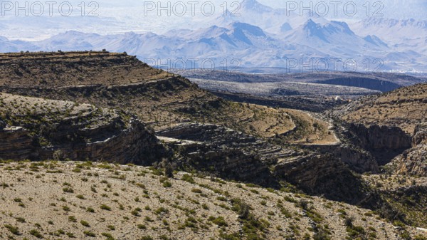 Slopes with barren vegetation and gorges, the mountains of the Hajar Mountains in the background, Arabian Peninsula, Sultanate of Oman