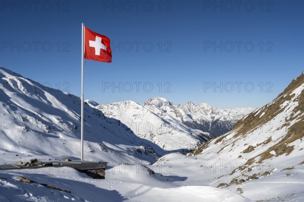 Swiss flag in front of mountain landscape in winter, mountain panorama with the peaks of the Bergüner Stöcke Tinzenhorn and Piz Ela, view at the Keschhütte in winter, Bündner Haute Route, Albula Alps, Rhaetian Alps, Grisons, Eastern Switzerland, Switzerland, Europe