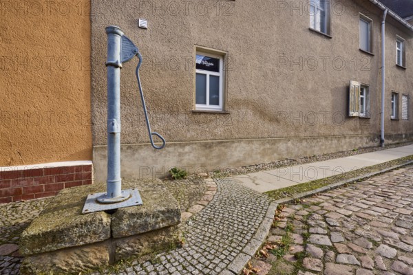 Historic pump, hand pump, pavement, cobblestones, facade with windows, Mühlberg Elbe, Elbe-Elster district, Brandenburg, Germany, Europe