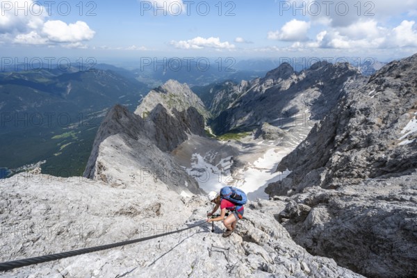 Mountaineer with helmet in a secured via ferrata, Zugspitze via ferrata, ascent to the Zugspitze, view of mountain basin with snow field of the Höllentalferner and Höllental, Wetterstein range, Wetterstein range, Bavaria, Germany, Europe