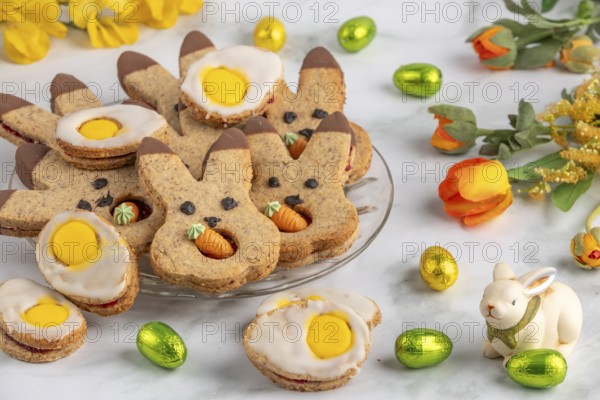 Bunny biscuits and egg biscuits decorated with icing next to Easter eggs and spring flowers