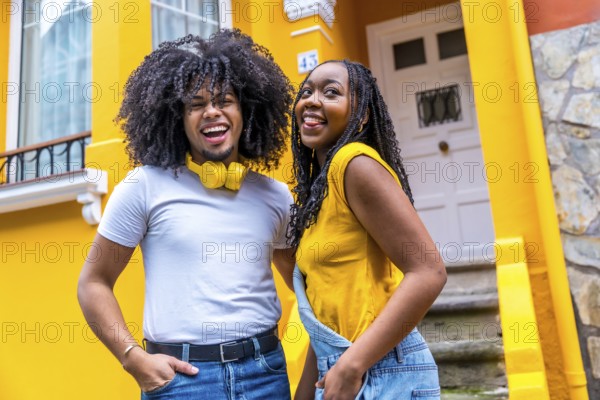 Portrait of a happy urban african couple smiling outdoors next to a house with yellow facade